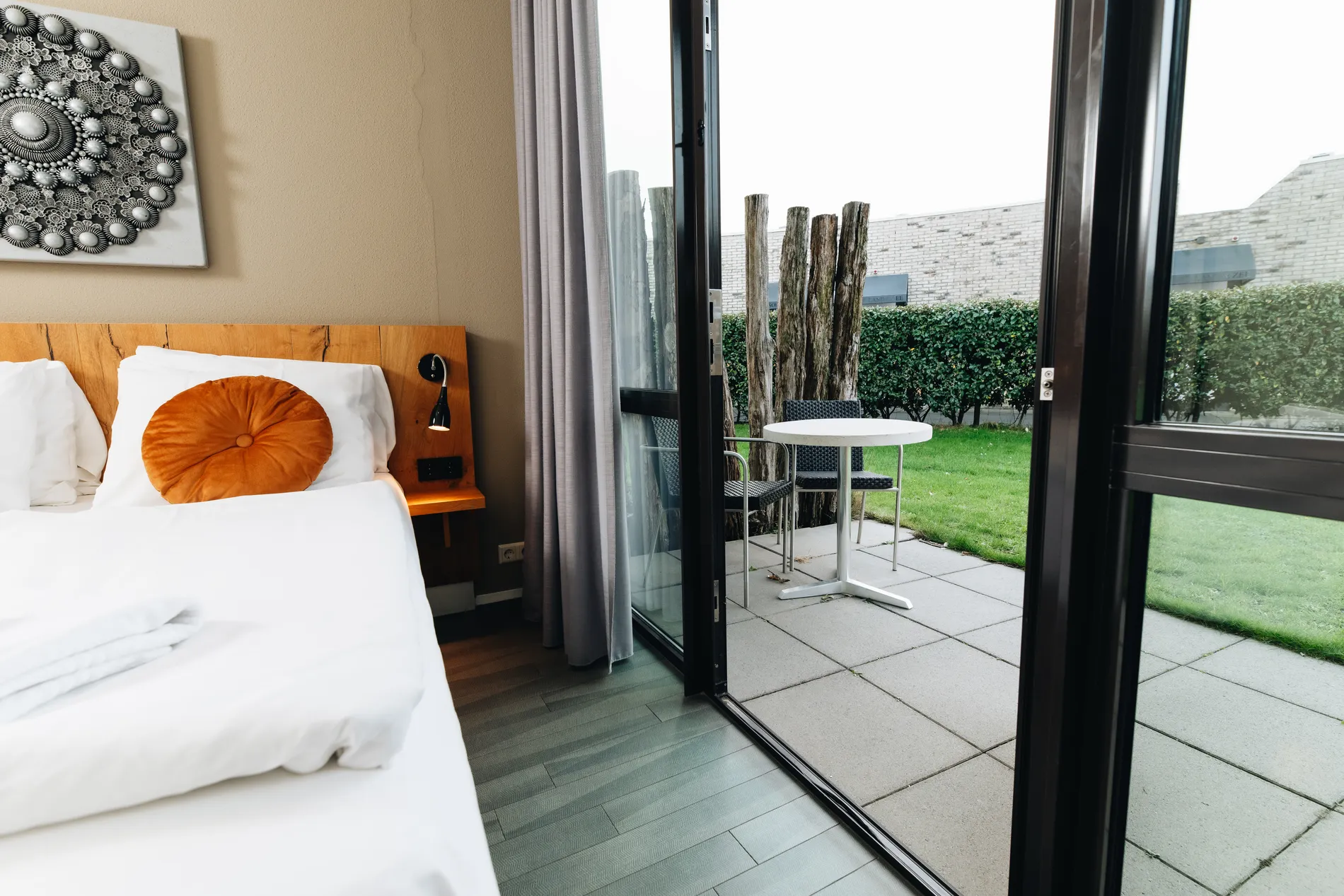 Privéterras met modern buitenmeubilair, houten afscheiding en zicht op het gazon, grenzend aan de hotelkamer.